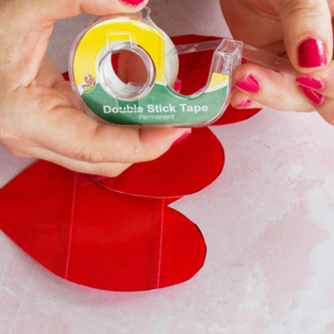 Two hands taping double sided tape on a duct tape heart